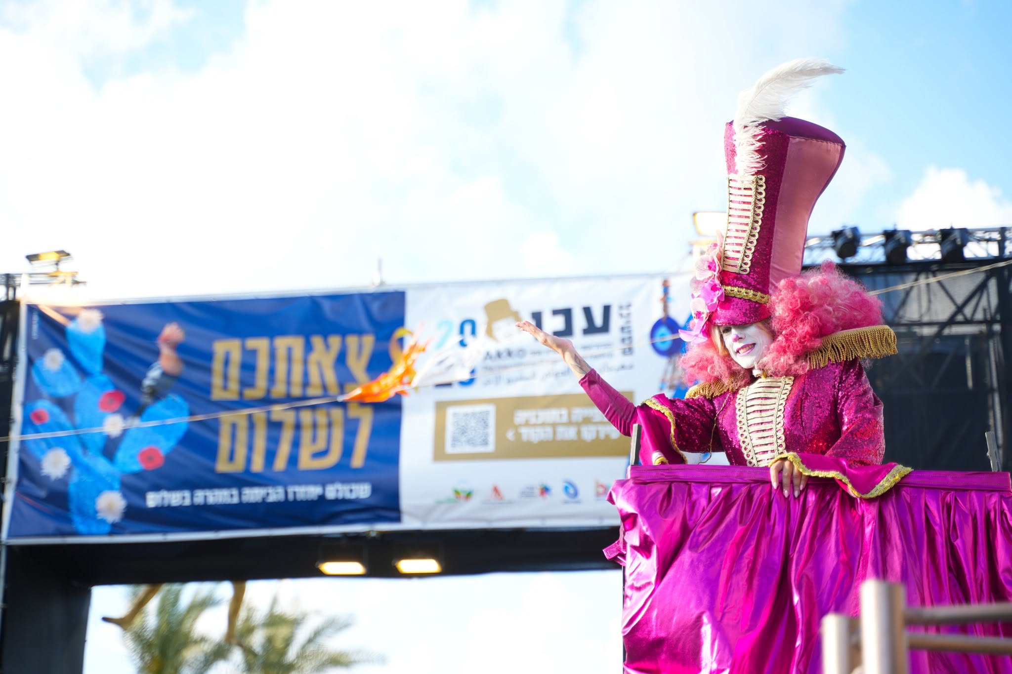 דמות ורודה גבוהה על קביים מופיעה ליד שילוט הפסטיבל.