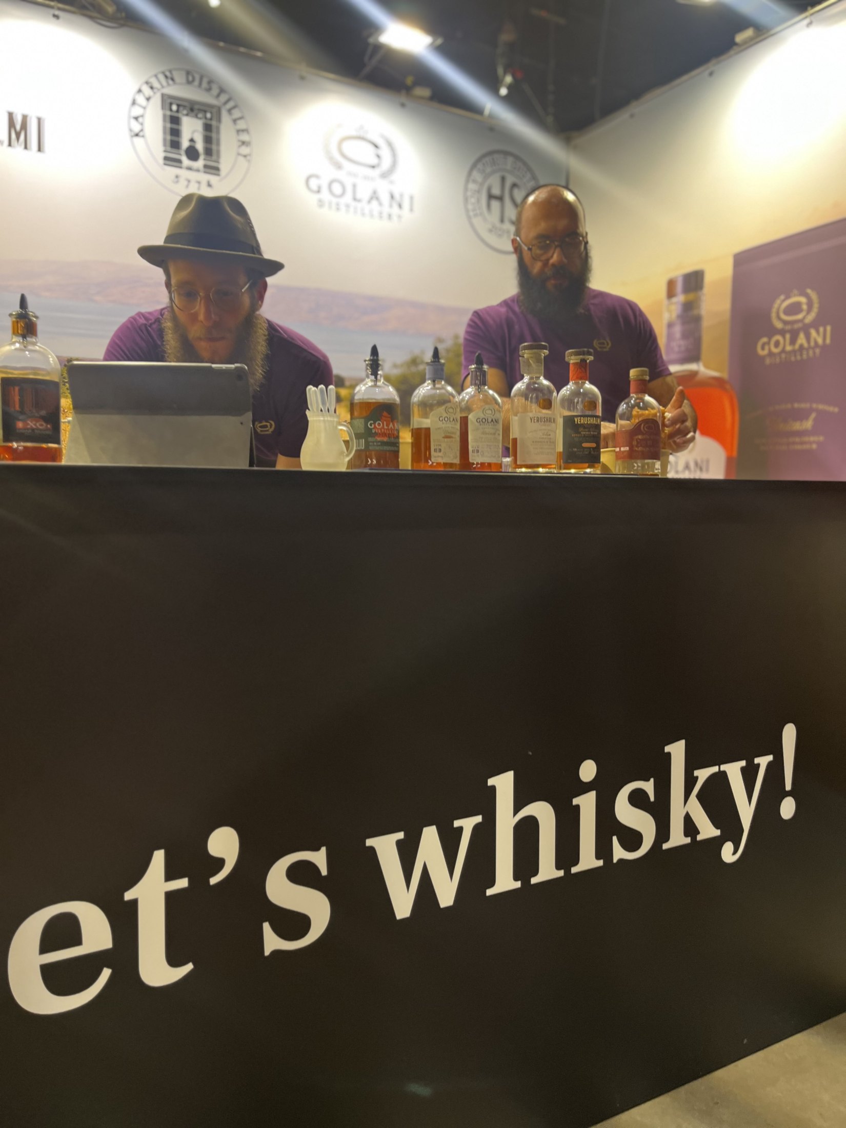 שני מציגים בדוכן משקאות עם שלט Let's Whisky.