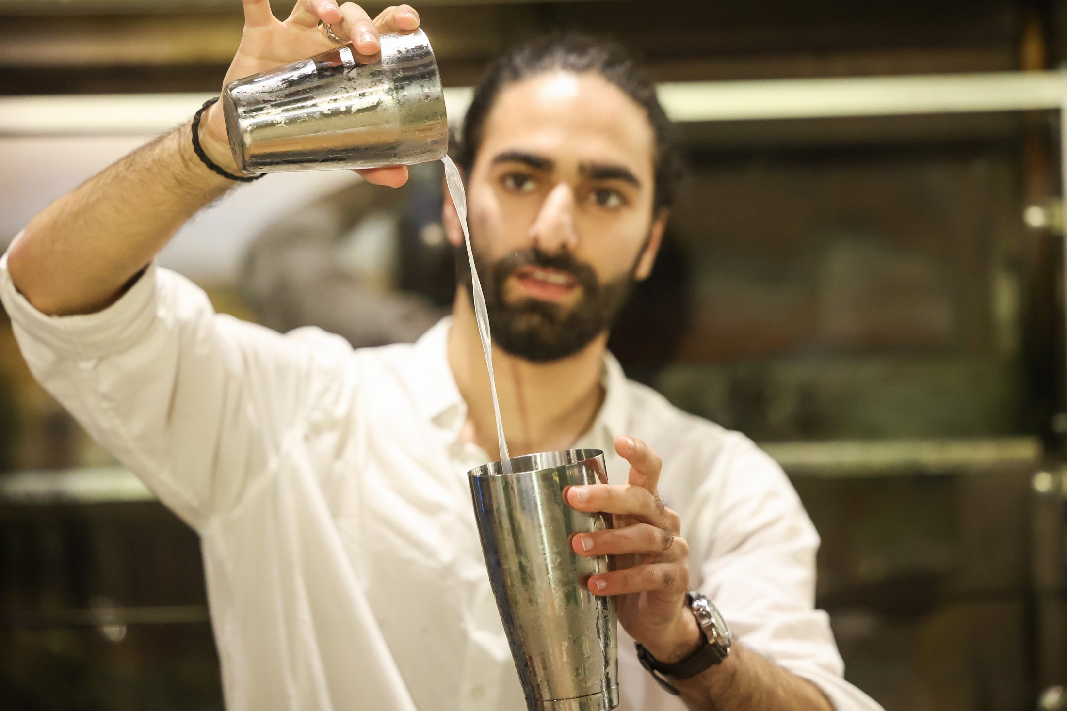 ברמן מוזג משקה בין שני כלי ערבוב.