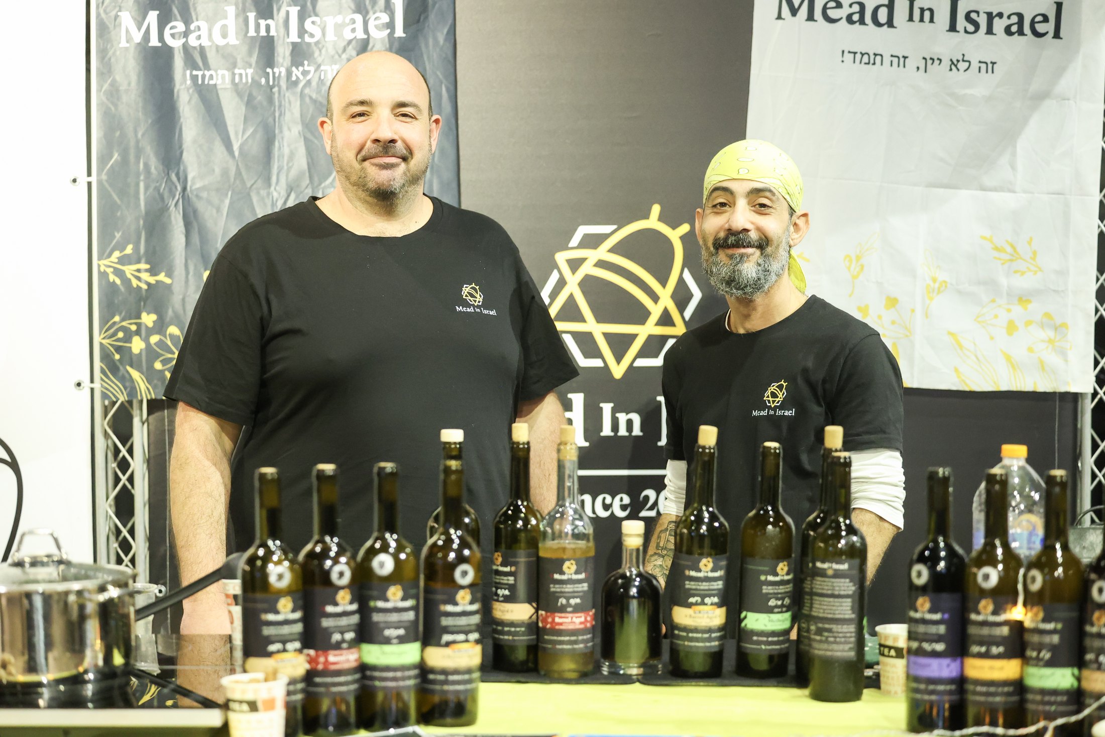 שני מציגים מחייכים מאחורי דוכן יין Mead in Israel.