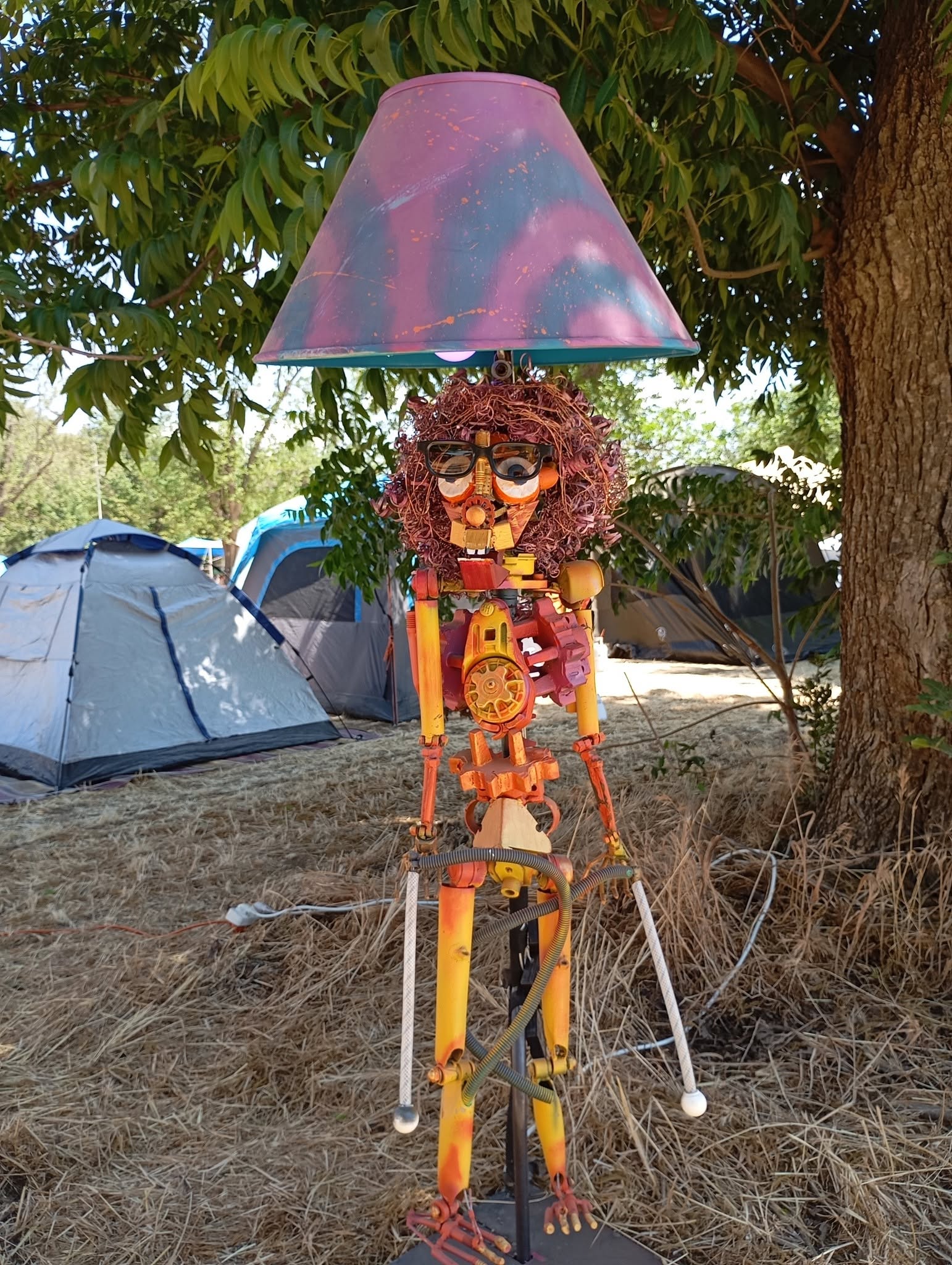 דמות פסל צבעונית עומדת תחת אהיל גדול לצד אוהלים.