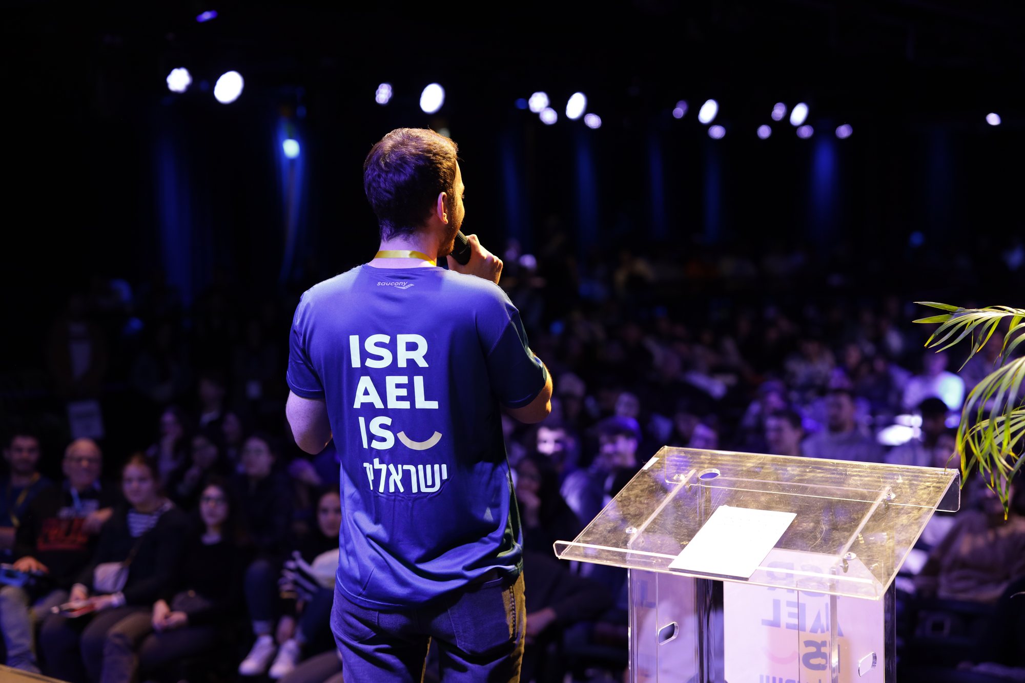 מבט מאחור על דובר בחולצת Israel-is מול הקהל.