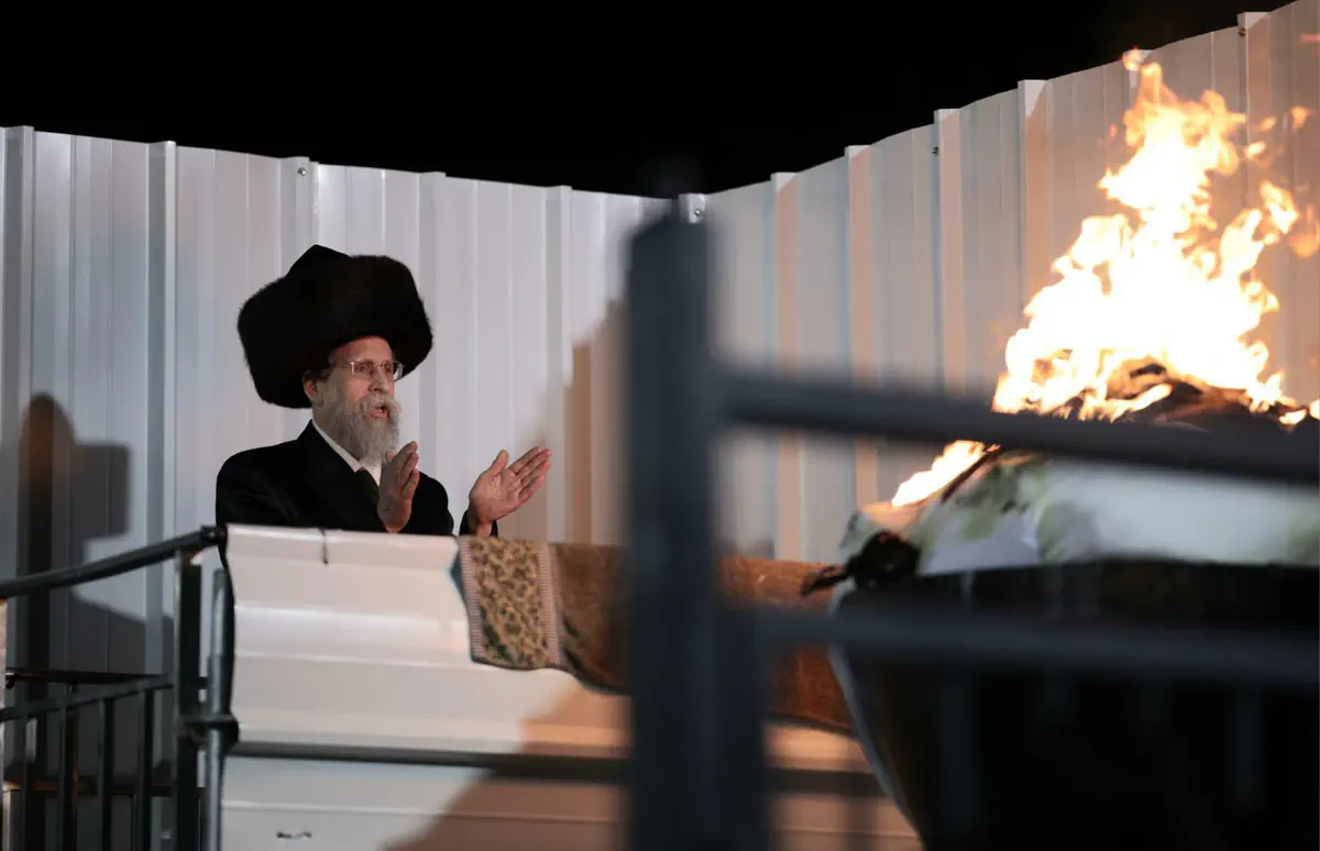רב בתלבושת חסידית עומד ליד האש במעמד ההדלקה.