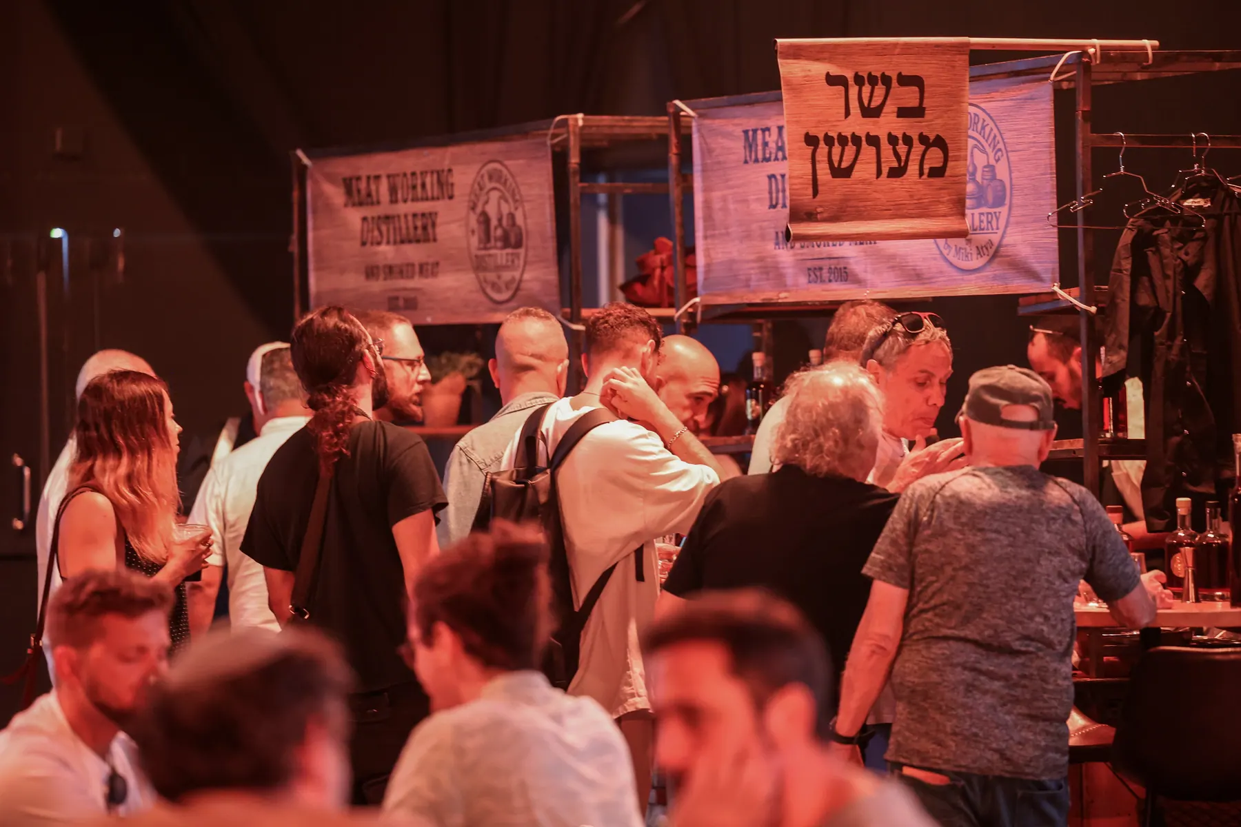 מבקרים מתקהלים סביב דוכני טעימה באולם.