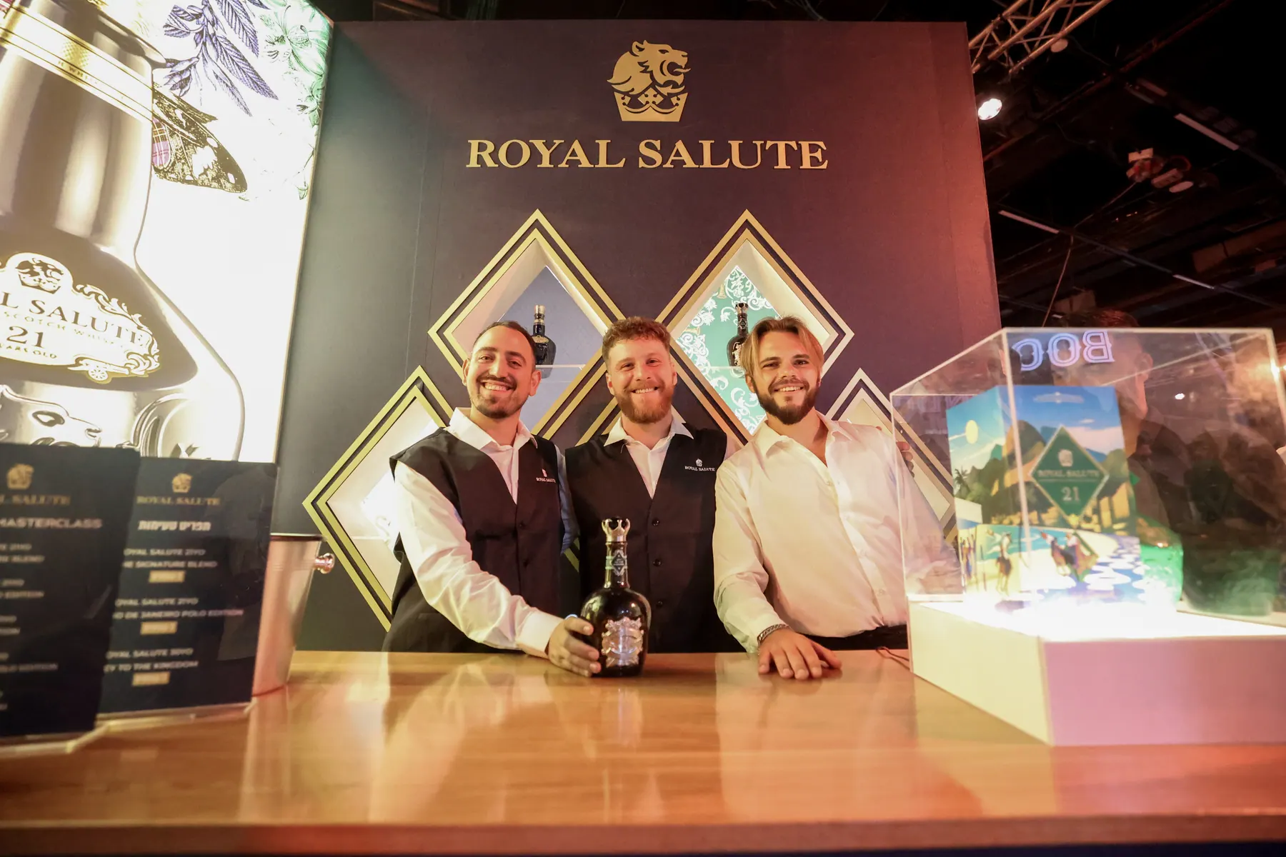 שלושה מציגים עומדים מאחורי דוכן Royal Salute.